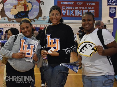 Photo of high school students showing off college swag from exhibitor tables.